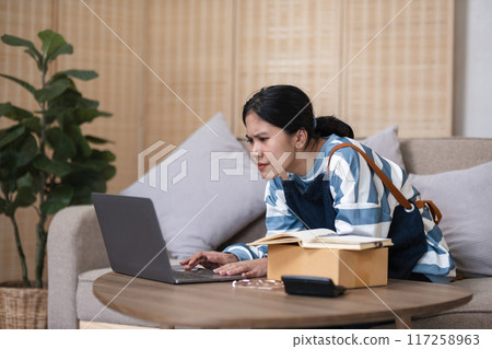 A small SME business owner feels tired while sitting on his home desk packing products into boxes. 117258963