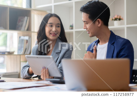 A young businessman and a female Asian accountant are discussing financial accounting and business planning together in the office. 117258977