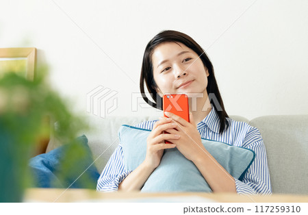 一個女人在客廳裡看著她的智能手機 一個女人在客廳裡看著她的智能手機 117259310