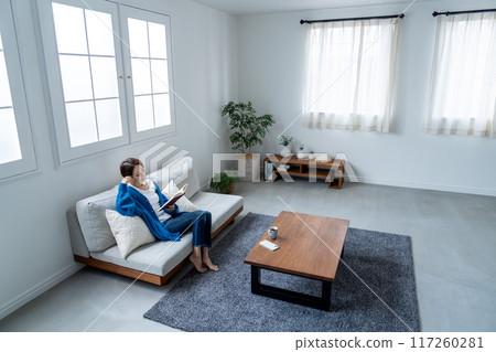 Middle-aged woman reading a book on the sofa 117260281