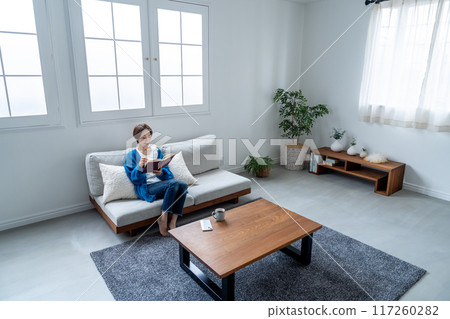 Middle-aged woman reading a book on the sofa Middle-aged woman reading a book on the sofa 117260282