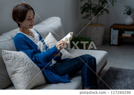 Middle-aged woman reading a book on the sofa Middle-aged woman reading a book on the sofa 117260290