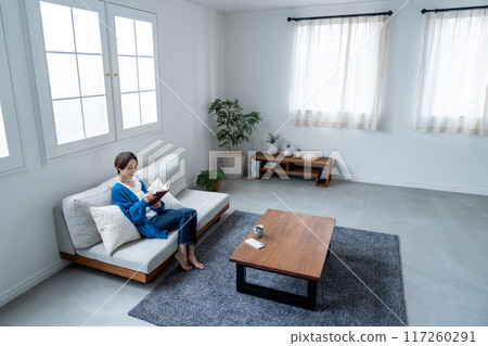 Middle-aged woman reading a book on the sofa Middle-aged woman reading a book on the sofa 117260291