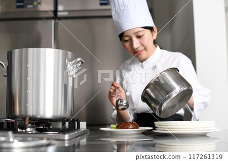 Young Asian female chef serving food on a plate Young Asian female chef serving food on a plate 117261319