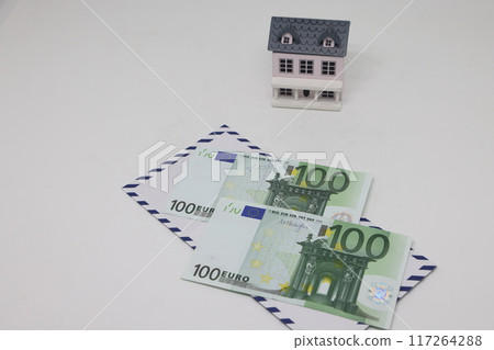 Banknotes in a white envelope and a toy house, funds for the purchase of real estate. Banknotes in a white envelope and a toy house, funds for the purchase of real estate. 117264288