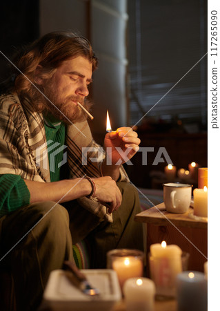 Lighting Cigarette Surrounded by Candles in Cozy Room 117265090