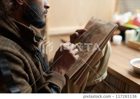 Sketching Man with Notebook in Hands Sitting Indoors 117265136