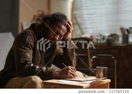 Concentrating on Writing at Wooden Desk in Cozy Room Concentrating on Writing at Wooden Desk in Cozy Room 117265158
