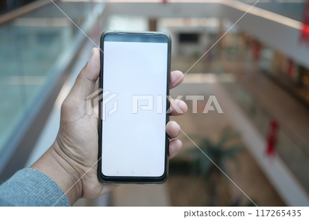 A person holds a blank smartphone in a modern indoor setting, highlighting contemporary design 117265435