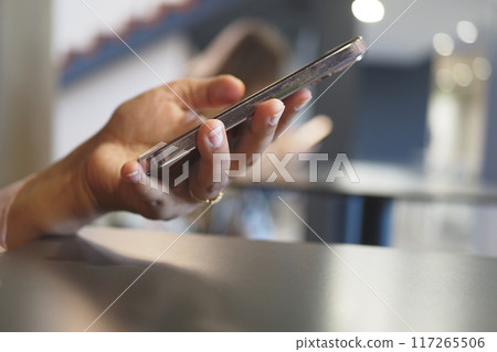 Hand Holding Smartphone in Modern Caf Setting Hand Holding Smartphone in Modern Caf Setting 117265506