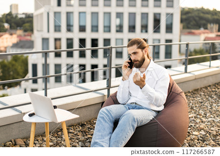 Man working remotely on rooftop while making a phone call 117266587