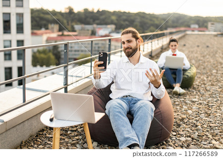 Young professionals working remotely on outdoor rooftop with devices 117266589