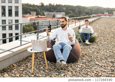 Businessmen working remotely on rooftop with laptops and smartphones 117266590