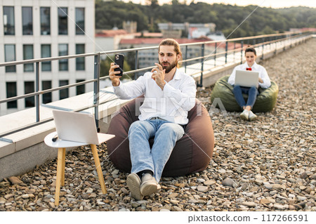 Remote workers on rooftop working with laptops and smartphones Remote workers on rooftop working with laptops and smartphones 117266591