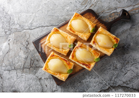 Delicious homemade Poached pears in puff pastry closeup on the wooden board. Horizontal top view Delicious homemade Poached pears in puff pastry closeup on the wooden board. Horizontal top view 117270033