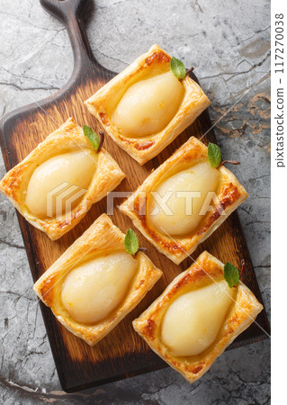 Poached Pear Puff Pastry with walnut filling and a sticky poaching liquid closeup on the wooden board. Vertical top view 117270038