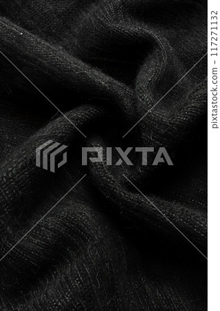 Close-up view of black fabric with woven texture folded in half. Intricate pattern and shadow create striking visual effect. Fabric appears smooth with subtle wrinkles on gray background. 117271132