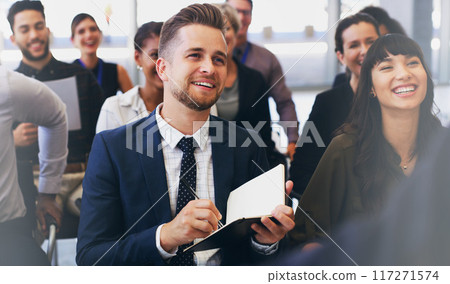 Please repeat that so I can make a note. Cropped shot of a handsome young businessman sitting with his colleagues and holding a notebook while in the office. 117271574
