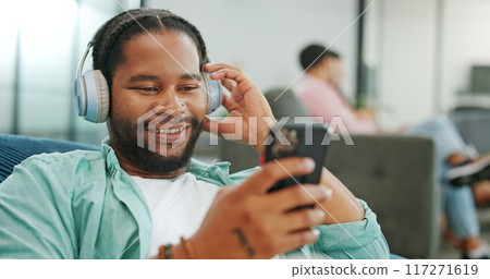 Headphones, relax and black man with a phone on a sofa in living room listening to music and chatting. Rest, chill and African guy streaming radio, album or playlist while relaxing on couch at home. 117271619