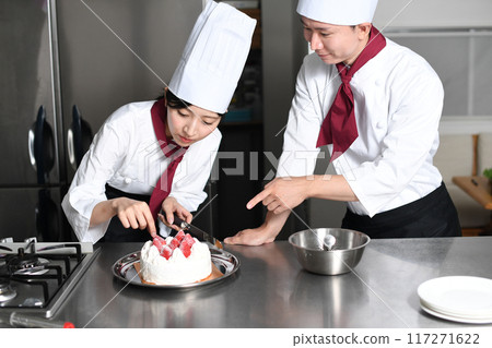 A female pastry chef making a cake and a man teaching her 117271622