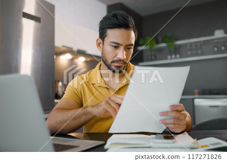 Budget, paperwork and Asian man planning with a laptop for finance, insurance and tax. Payment, note and Japanese entrepreneur reading information on a contract to start a small business from home 117271826