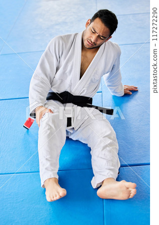 Sports, injury and pain in legs on karate fitness dojo floor for tournament, training or workout. Professional athlete uniform of martial arts man with knee pain or arthritis at sport club. 117272290