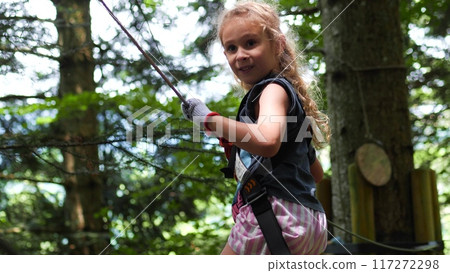 Happy little blonde girl walks along outdoor climbing park trail in the forest 117272298