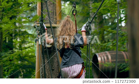 Little blonde girl walks along outdoor climbing park trail in the forest Little blonde girl walks along outdoor climbing park trail in the forest 117272300