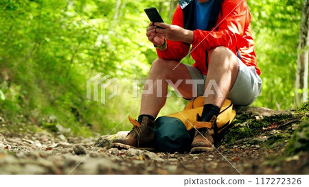 Male hiker uses his smartphone while having a rest in the woods 117272326