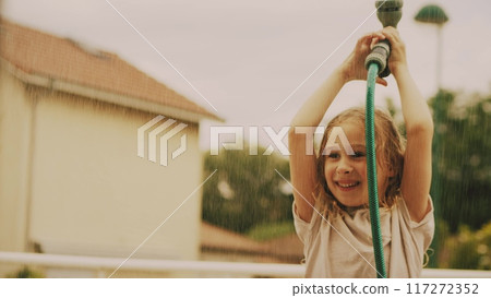 Happy little girl sprinkle water with a water sprinkler hose on a hot summer day, vacation time, slow motion Happy little girl sprinkle water with a water sprinkler hose on a hot summer day, vacation time, slow motion 117272352