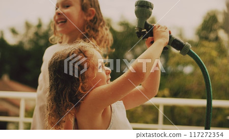 Little girls have fun with a water sprinkler hose on a hot summer day at home, slow motion Little girls have fun with a water sprinkler hose on a hot summer day at home, slow motion 117272354