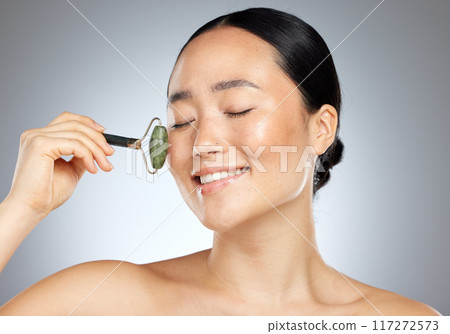 Beauty, skincare and woman facial roller or dermatology tool for healthy and smooth skin against studio background. Happy girl or asian model do massage routine for wellness, health and cosmetics Beauty, skincare and woman facial roller or dermatology tool for healthy and smooth skin against studio background. Happy girl or asian model do massage routine for wellness, health and cosmetics 117272573