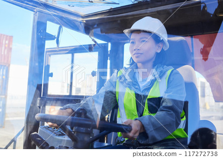 Supply chain, logistics and transport with a woman shipping worker driving a vehicle on a commercial container dock. Freight, cargo and stock with an asian female courier at work in the export trade Supply chain, logistics and transport with a woman shipping worker driving a vehicle on a commercial container dock. Freight, cargo and stock with an asian female courier at work in the export trade 117272738