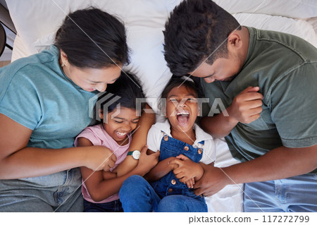 Family, children and love above parents ticking a girl and her sister in the bed in a bedroom of the home together. Happy, smile and laugh with a mother and father tickling their daughters from above 117272799