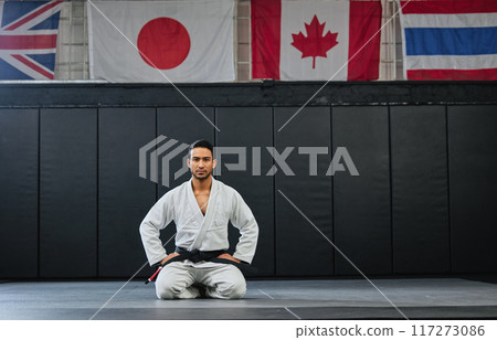 Martial arts, black belt and sitting fighter inside dojo for training. Defence club, champion or coach exercising in his sportswear. Karate or mma man looking with focus and discipline at the gym. 117273086