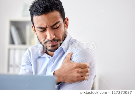 Bad muscle pain in the arm, shoulder and body after an injury and ache while working in the office. Angry, upset and frustrated businessman with a painful strain, hurt and sore sitting at his desk 117273087