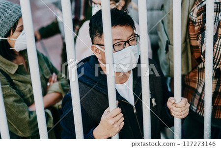 Sick, trapped young covid patient stuck in the city feeling like a prisoner, wearing a medical face mask. Foreign asian man in a crowd during a pandemic. Male following city healthcare safety rules. Sick, trapped young covid patient stuck in the city feeling like a prisoner, wearing a medical face mask. Foreign asian man in a crowd during a pandemic. Male following city healthcare safety rules. 117273146