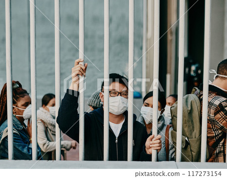 Behind bars, lockdown and covid restrictions with a man wearing a mask during a pandemic and travel ban. Portrait of a male being locked out during the international or global corona virus outbreak Behind bars, lockdown and covid restrictions with a man wearing a mask during a pandemic and travel ban. Portrait of a male being locked out during the international or global corona virus outbreak 117273154
