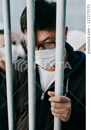 Lockdown, isolation and covid travel ban with a man in a mask behind bars during an international pandemic. Corona virus restrictions, feeling like a prisoner or captive during a global shutdown 117273155