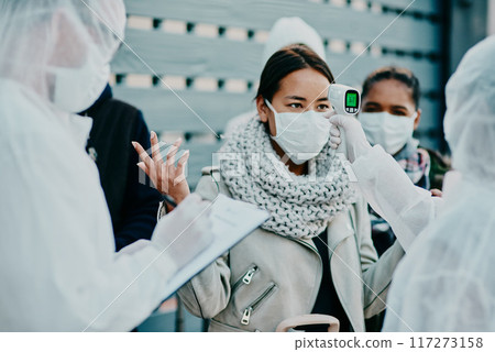 Health care worker scanning a frustrated woman temperature for corona with a thermometer. Concerned female made victim of racial profiling, looking annoyed and angry during the pandemic 117273158