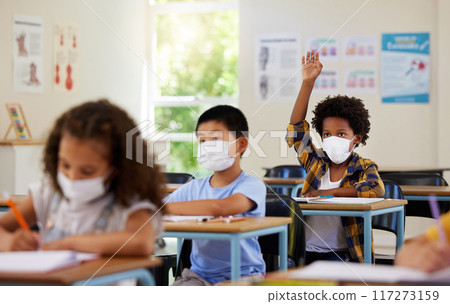 Covid, students and education children in school classroom raising hand to answer, ask or question lesson with classmates. Diverse group of kids, boys or girls with face masks learning in study class 117273159