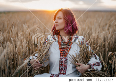 Ukrainian woman in traditional ethnic dress sitting in wheat field at sunset Ukrainian woman in traditional ethnic dress sitting in wheat field at sunset 117274787