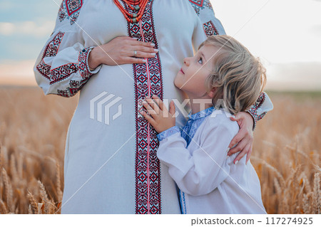 Pregnant Ukrainian Mom With Son In Wheat Field, On Nature. Happy Smiling Boy Brother Touching mothers bump tummy. 117274925