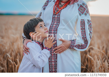 Pregnant Ukrainian Mom With Son In Wheat Field, On Nature. Happy Smiling Boy Brother Touching mothers bump tummy. 117274930