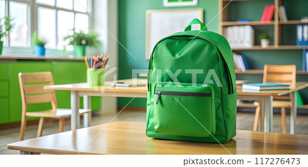 A green school backpack sits on a wooden desk 117276473