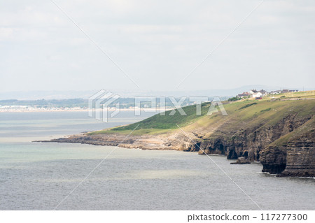 A cliff with a pebbly coastline and layers of rock eroded by seawater visible in the suburbs of South Wales 117277300