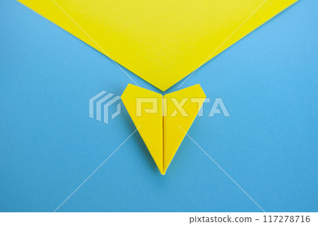 Close up top view view of yellow paper airplane flying along the route on blue background Close up top view view of yellow paper airplane flying along the route on blue background 117278716