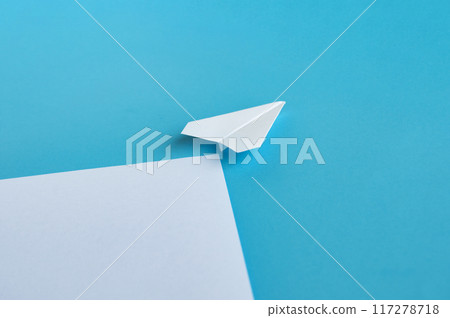 Angle view of white paper airplane flying along the route on blue background with customizable space for text Angle view of white paper airplane flying along the route on blue background with customizable space for text 117278718