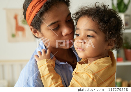 Mother embracing her child, holding lovingly while standing in cozy room setting with animal posters on wall, capturing genuine moment of maternal care and connection 117279258