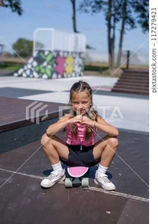 Cute funny curly-haired girls sitting on a skateboard on the pyramid of the skatepark Cute funny curly-haired girls sitting on a skateboard on the pyramid of the skatepark 117279421